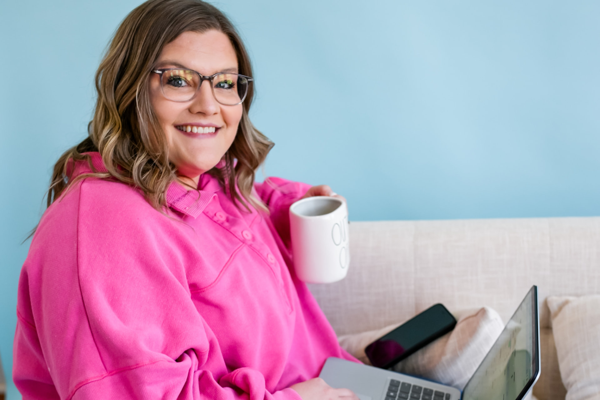 Shelby smiling with a cup of coffee while working on her laptop